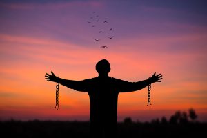 Silhouette of young man standing alone  with beautiful sky at sunset open both arms with chains on his arms. He felt free from the shackles tied to his arms.